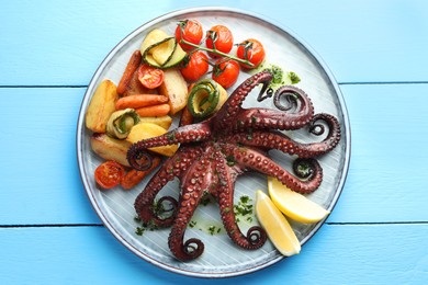Photo of Fried octopus with herb sauce, lemon and vegetables on light blue wooden table, top view