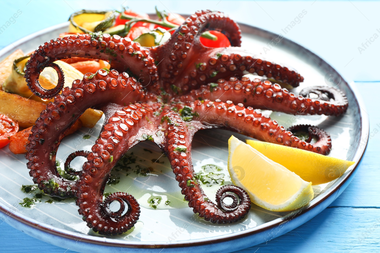 Fried octopus with herb sauce, lemon and vegetables on light blue wooden table, closeup Photo of Fried octopus with herb sauce, lemon and vegetables on light blue wooden table, closeup