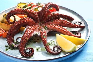 Photo of Fried octopus with herb sauce, lemon and vegetables on light blue wooden table, closeup