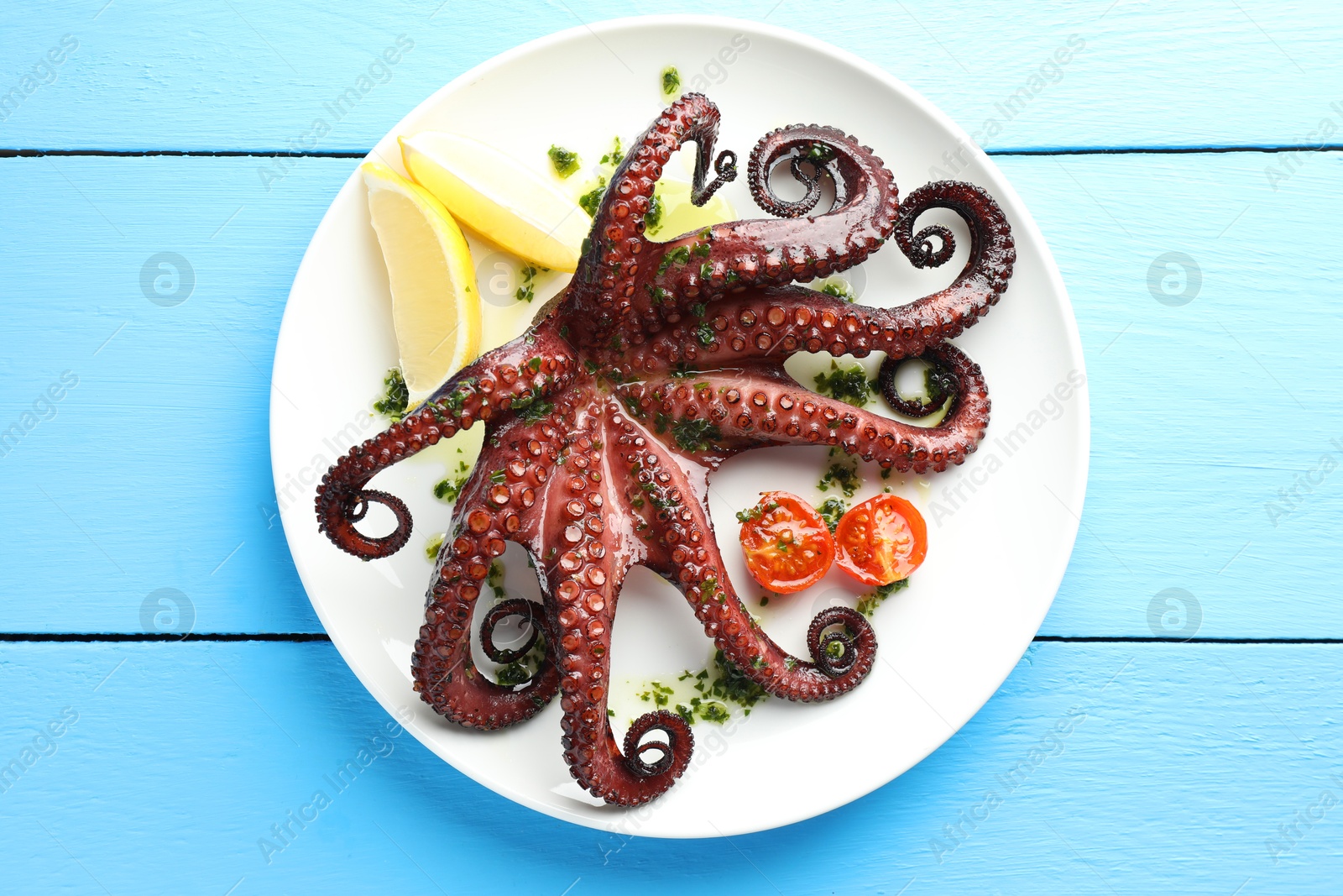 Fried octopus with herb sauce, lemon and tomatoes on light blue wooden table, top view Photo of Fried octopus with herb sauce, lemon and tomatoes on light blue wooden table, top view