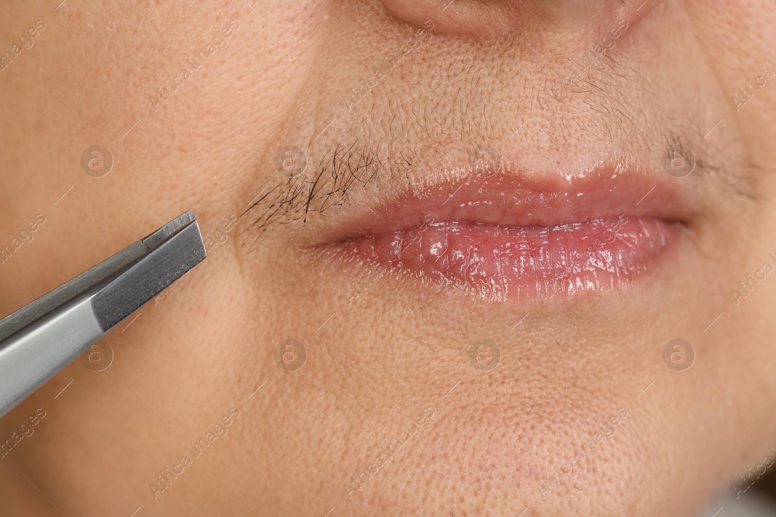 Photo of Senior woman plucking her mustache with tweezers, closeup