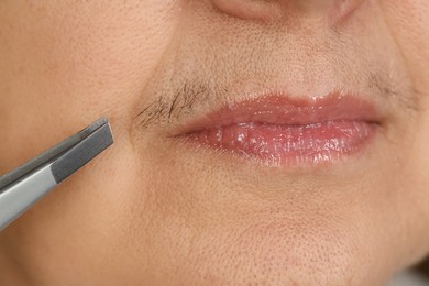 Senior woman plucking her mustache with tweezers, closeup