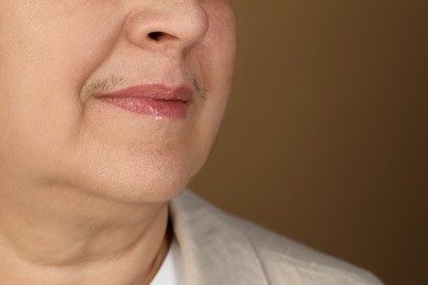 Photo of Senior woman with mustache on brown background, closeup. Space for text