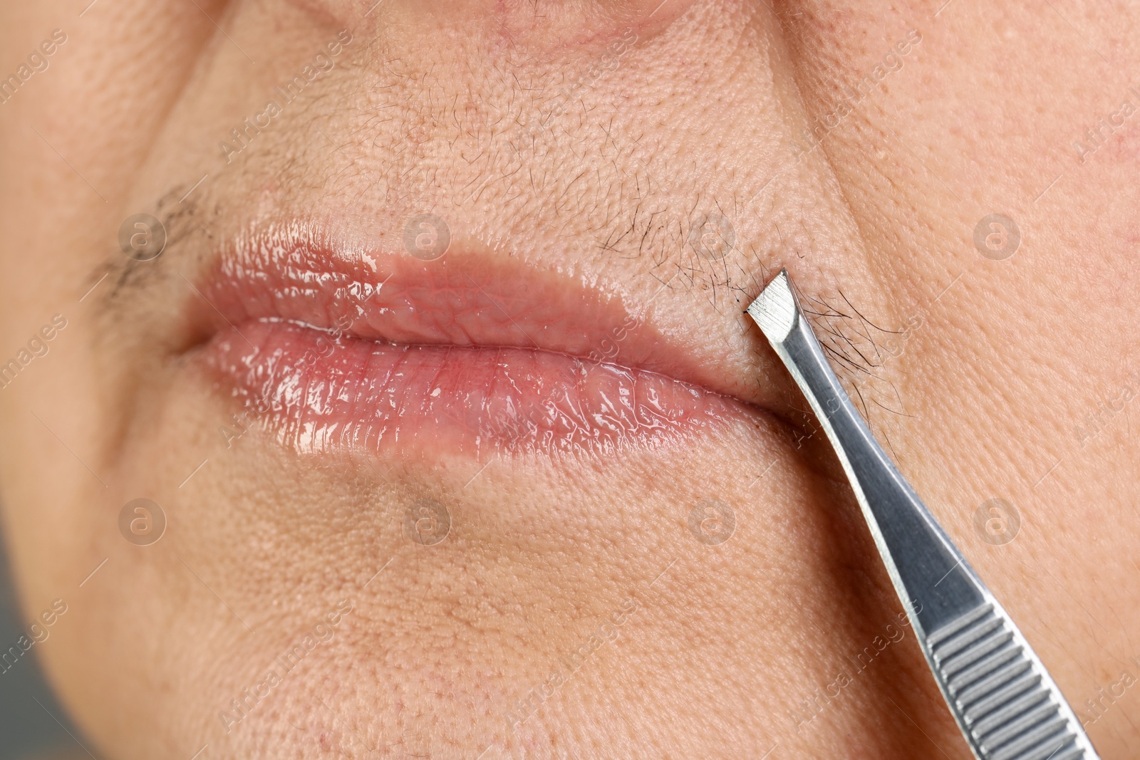 Photo of Senior woman plucking her mustache with tweezers, closeup