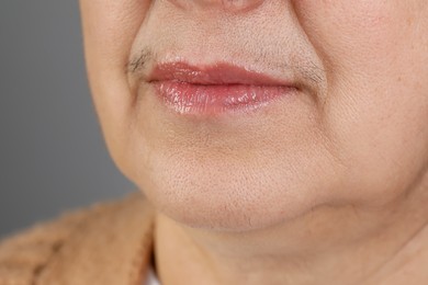 Senior woman with mustache on grey background, closeup