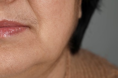 Senior woman with mustache on grey background, closeup