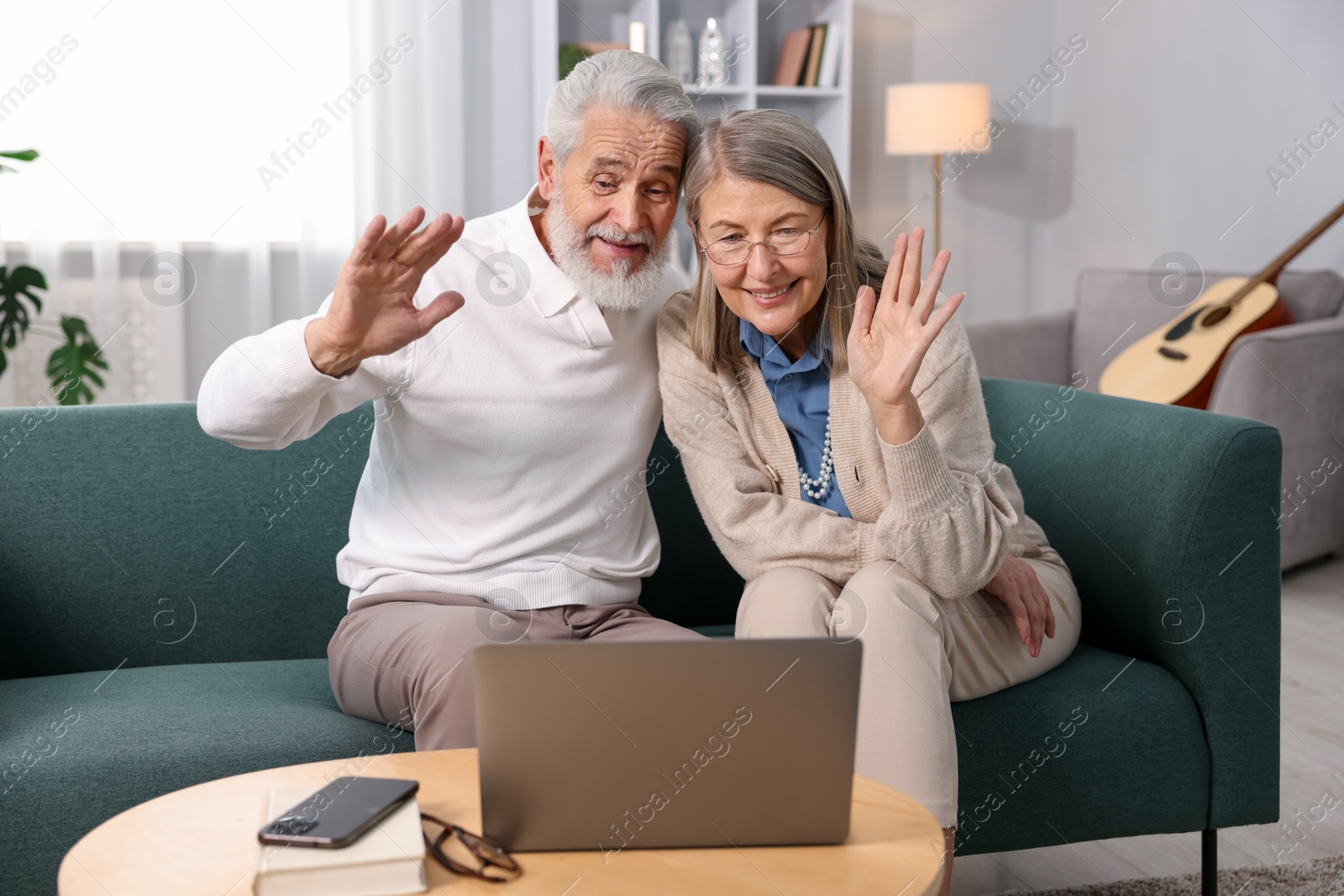 Photo of Happy elderly couple having video call by laptop on sofa at home