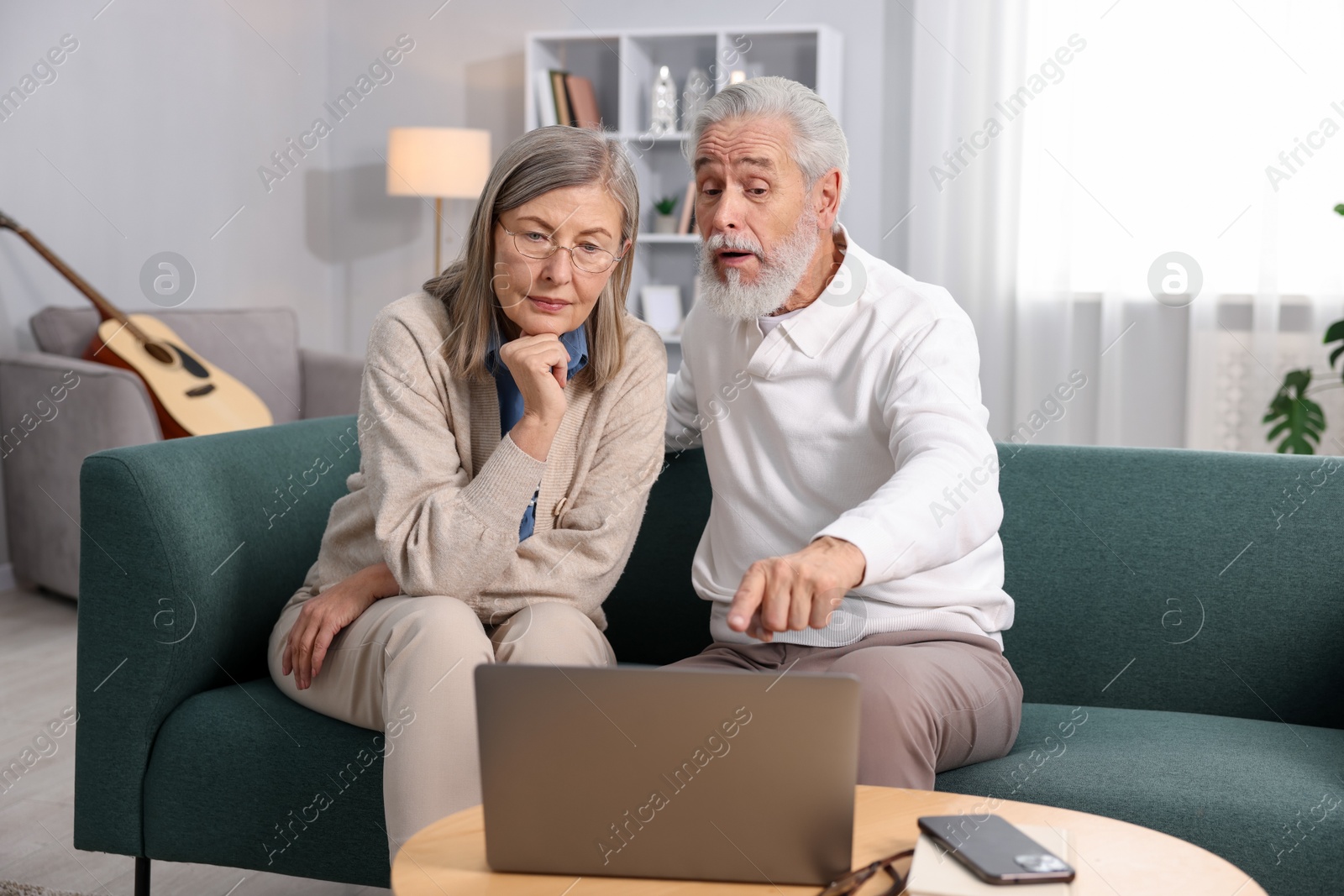 Photo of Cute elderly couple looking at laptop on sofa at home