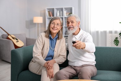 Photo of Happy elderly couple watching tv on sofa at home