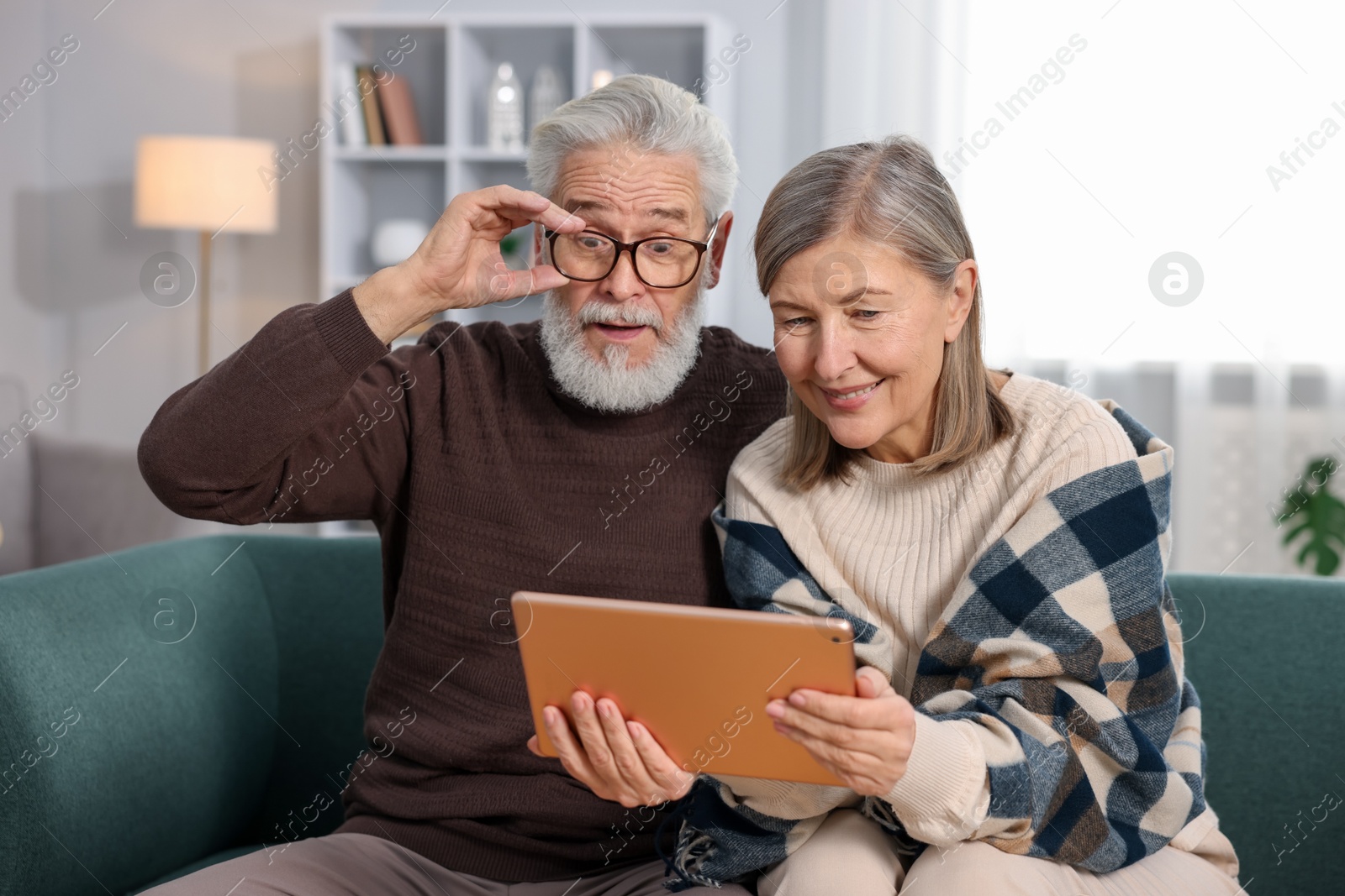 Photo of Cute elderly couple looking at tablet on sofa at home