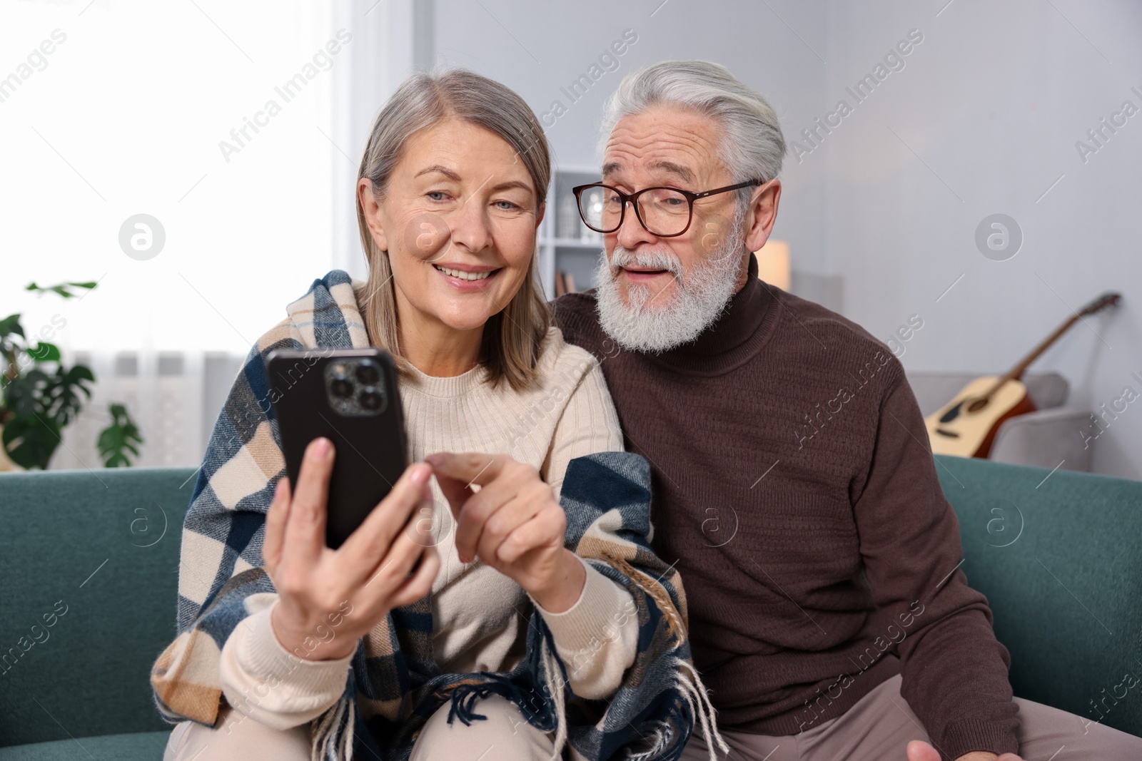 Photo of Happy elderly couple looking at smartphone on sofa at home