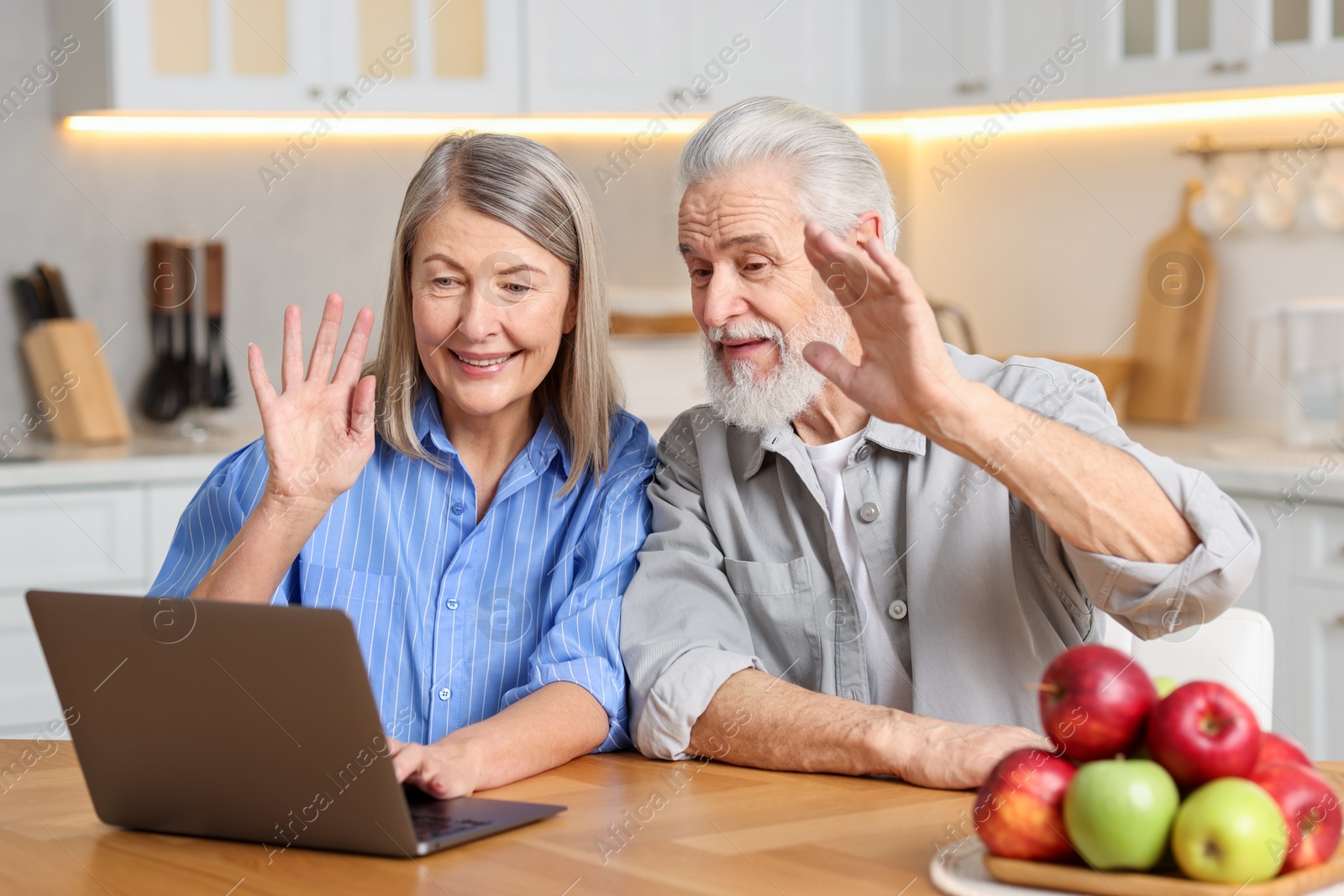 Photo of Happy elderly couple having video call by laptop at table in kitchen