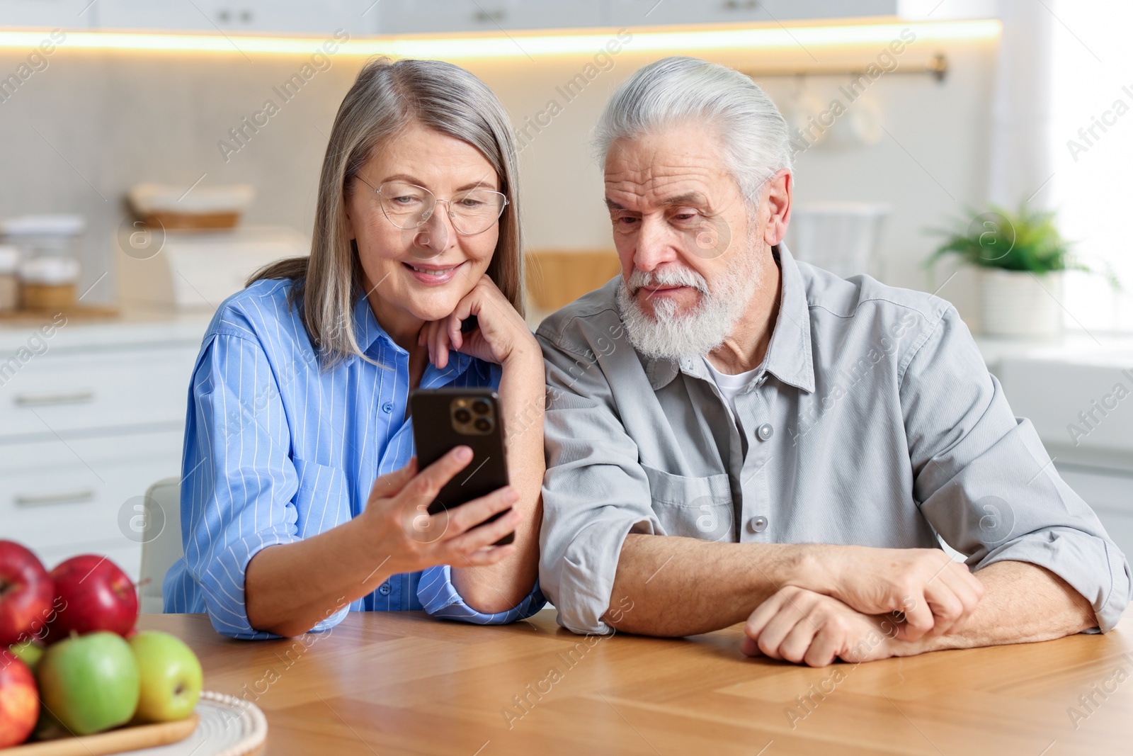 Photo of Cute elderly couple with smartphone at table in kitchen