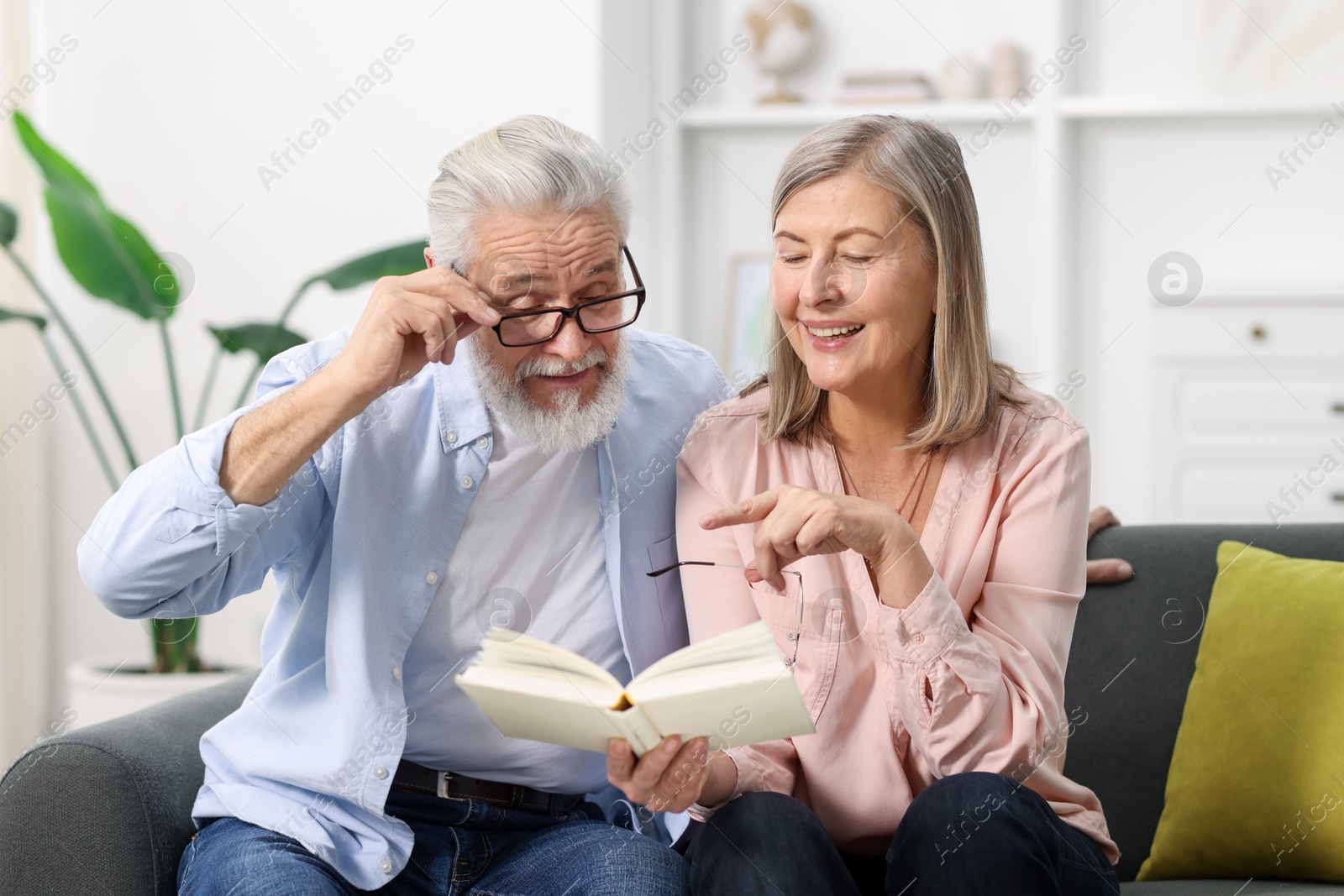 Photo of Happy elderly couple reading book together on sofa at home