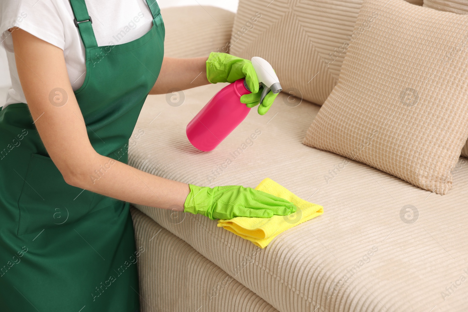 Photo of Janitor cleaning sofa with rag at home, closeup