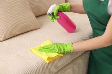 Photo of Janitor cleaning sofa with rag at home, closeup