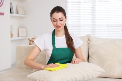 Photo of Janitor cleaning sofa with rag at home