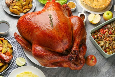 Whole baked turkey and other dishes served on grey table, closeup