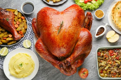 Whole baked turkey and other dishes served on grey table, flat lay