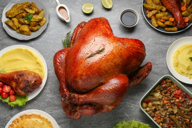 Whole baked turkey and other dishes served on grey table, flat lay