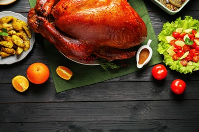 Whole baked turkey and other dishes served on black wooden table, flat lay. Space for text