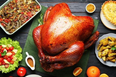 Photo of Whole baked turkey and other dishes served on black wooden table, flat lay