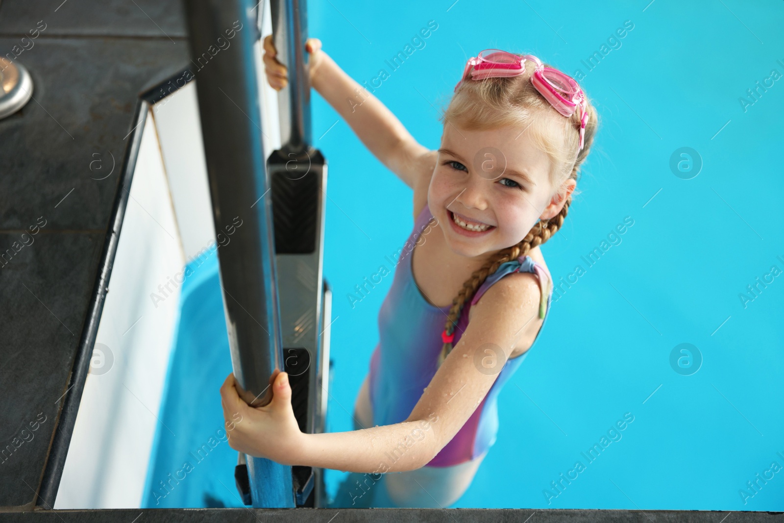 Photo of Little girl with goggles getting out of swimming pool indoors, space for text