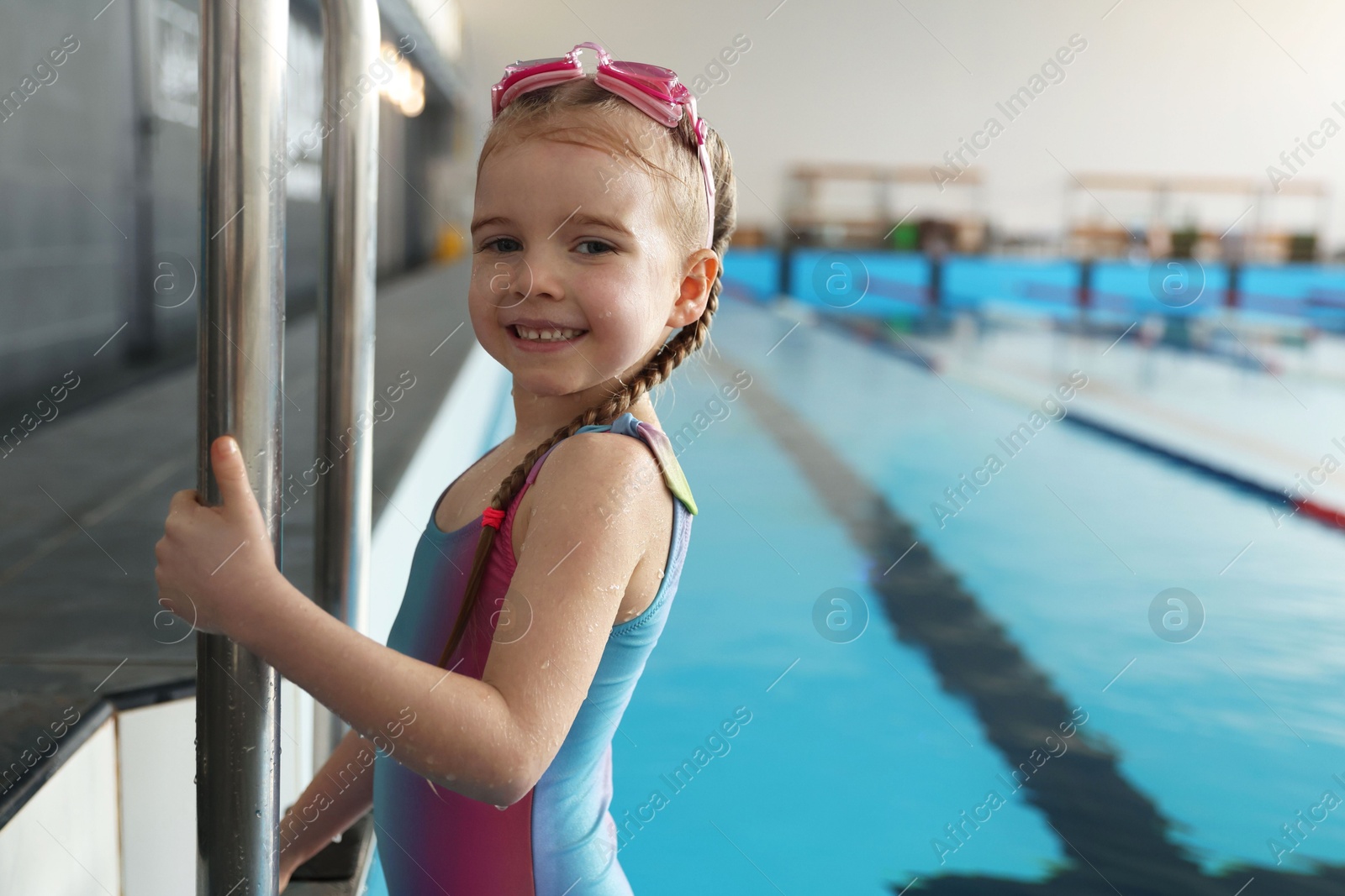 Photo of Little girl with goggles getting out of swimming pool indoors, space for text