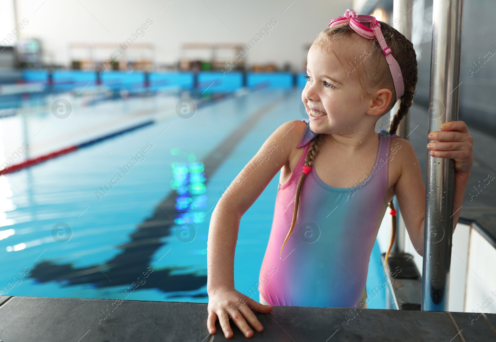 Photo of Little girl with goggles getting out of swimming pool indoors, space for text