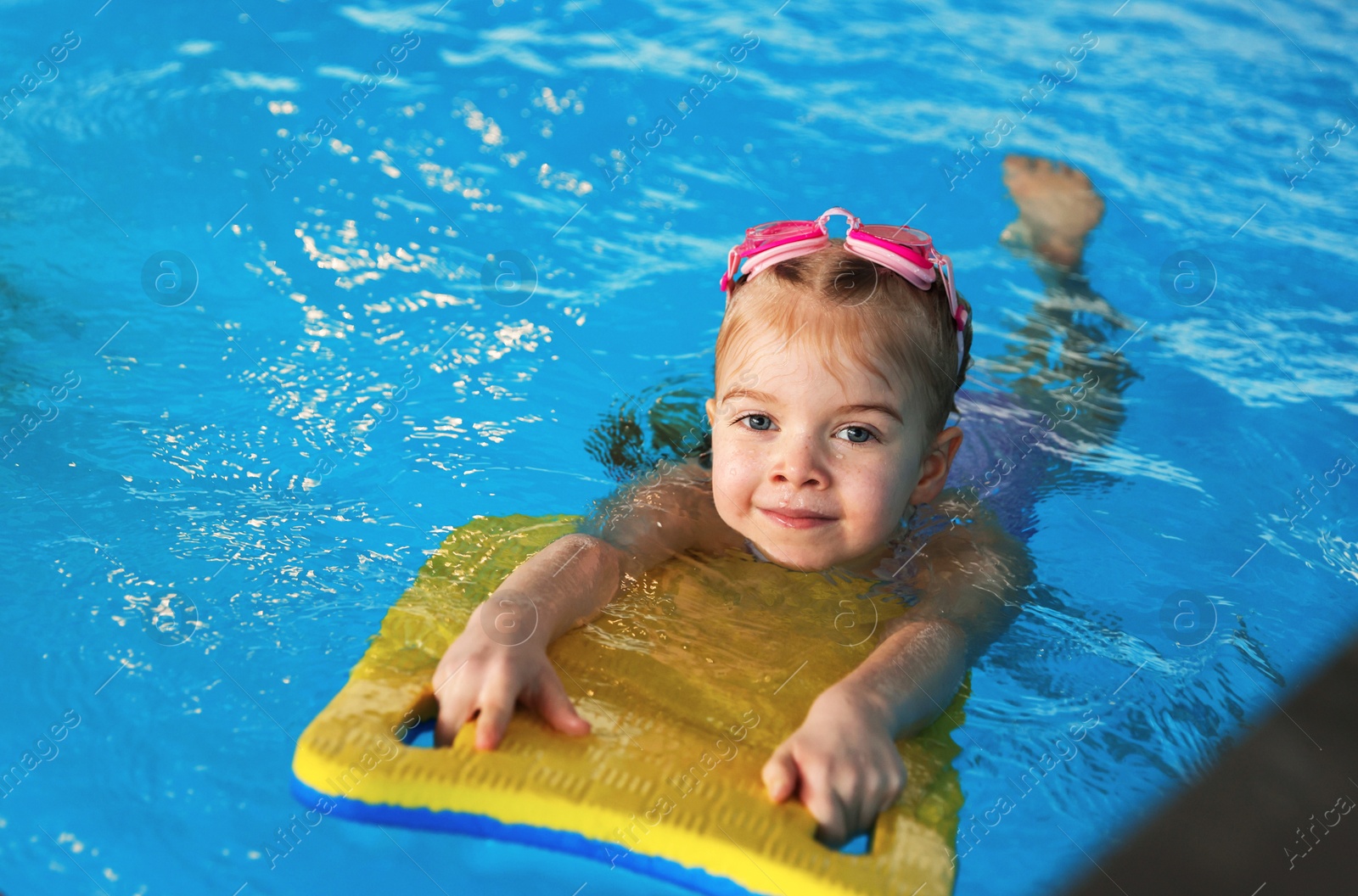 Photo of Little girl with goggles and kickboard swimming in pool indoors