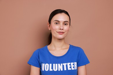 Photo of Young beautiful woman wearing t-shirt with printed word Volunteer on light brown background