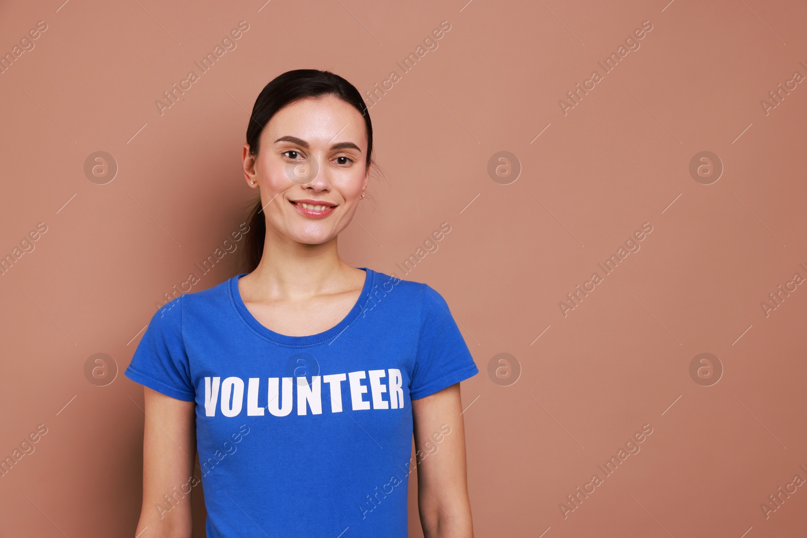 Photo of Young beautiful woman wearing t-shirt with printed word Volunteer on light brown background. Space for text