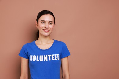 Young beautiful woman wearing t-shirt with printed word Volunteer on light brown background. Space for text