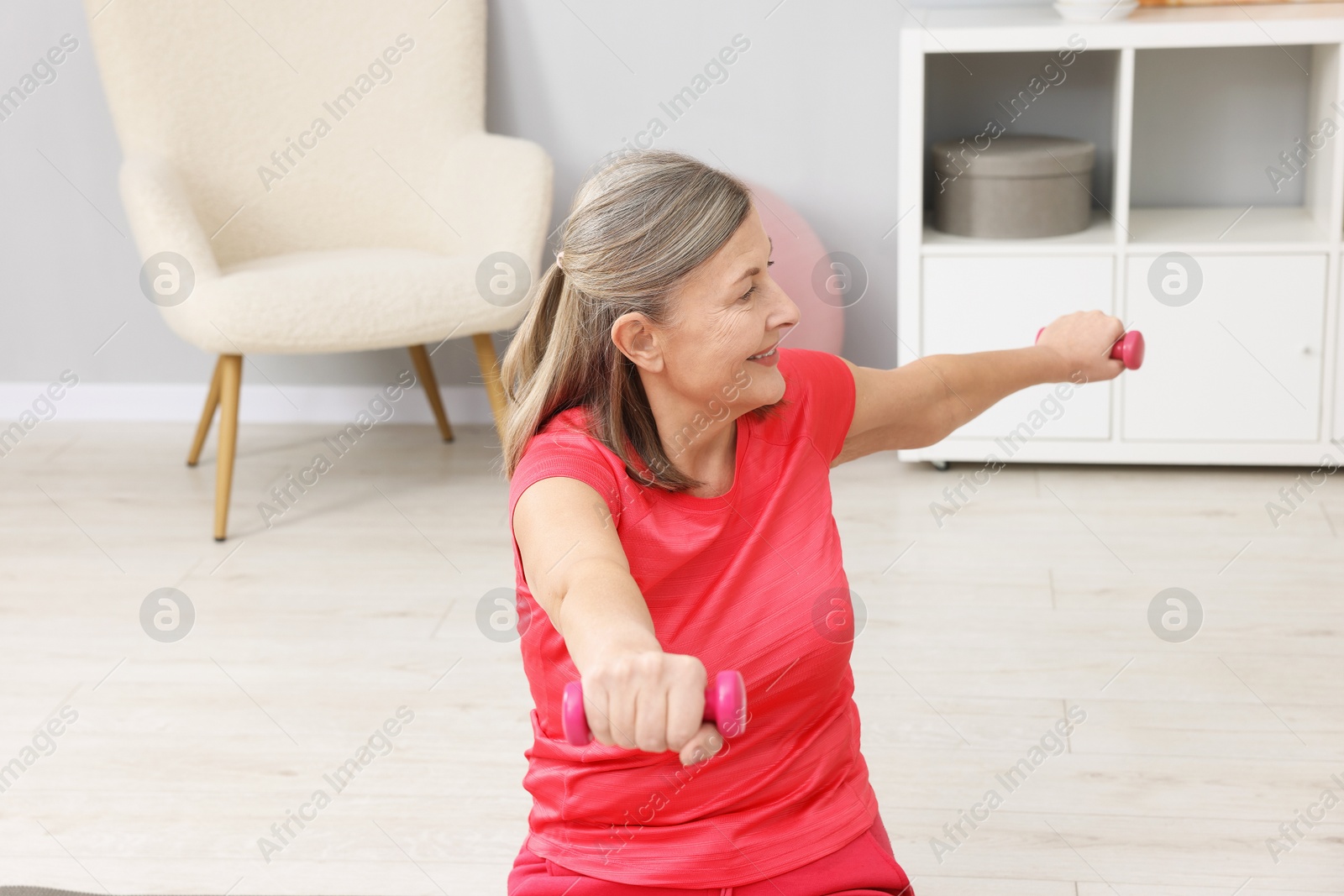 Photo of Smiling elderly woman exercising with dumbbells at home