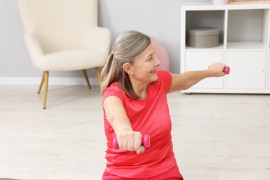 Smiling elderly woman exercising with dumbbells at home