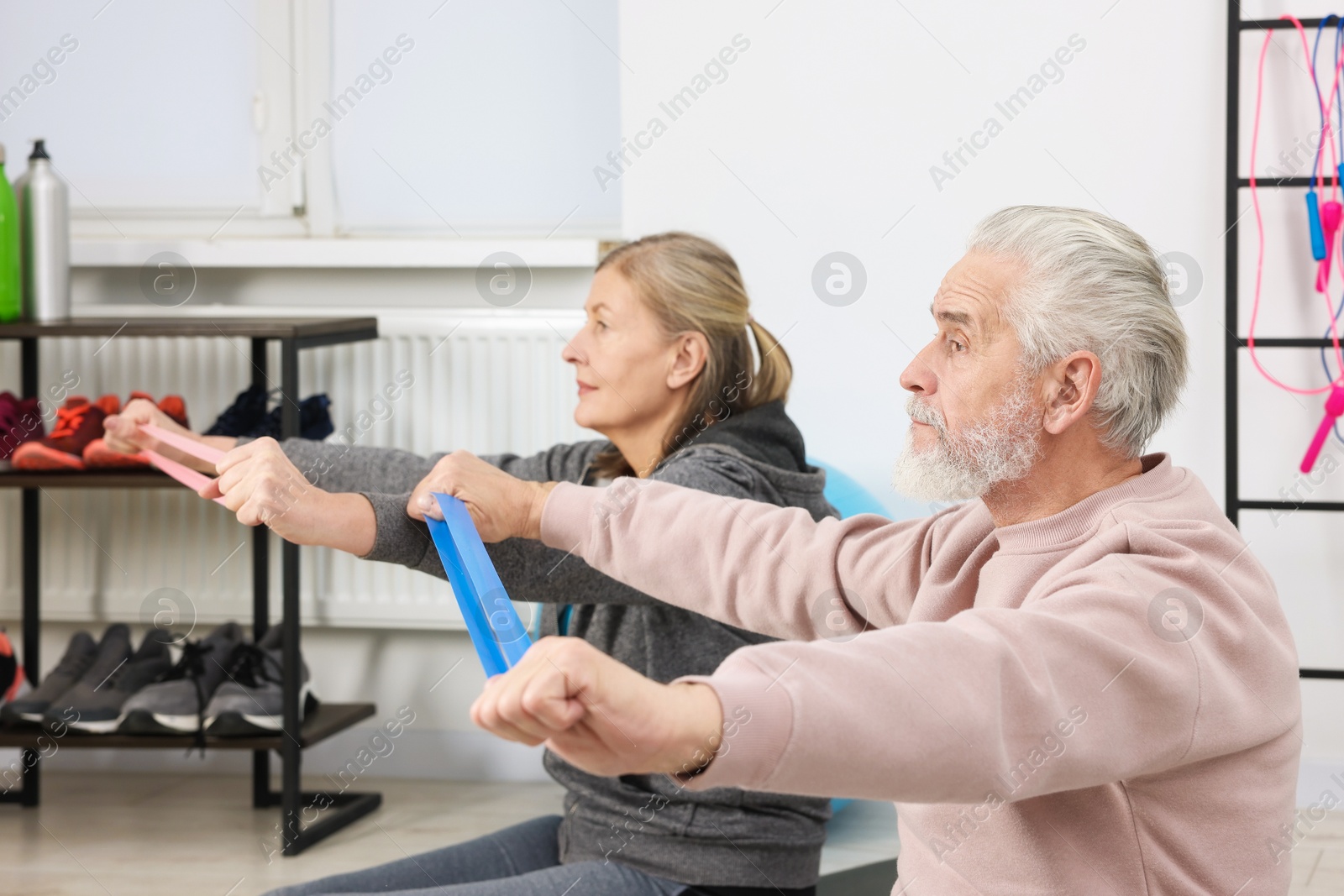 Photo of Elderly couple exercising with fitness elastic bands at home