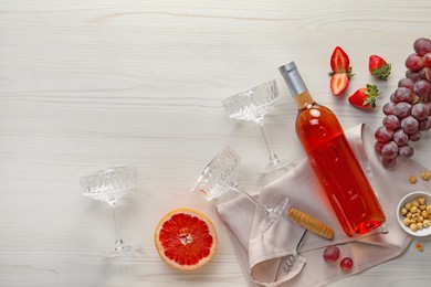 Flat lay composition with tasty rose wine in bottle and berries on light wooden table. Space for text