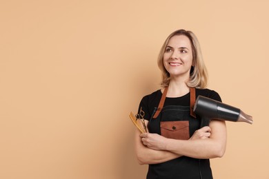 Smiling hairdresser with dryer, scissors and comb on beige background, space for text