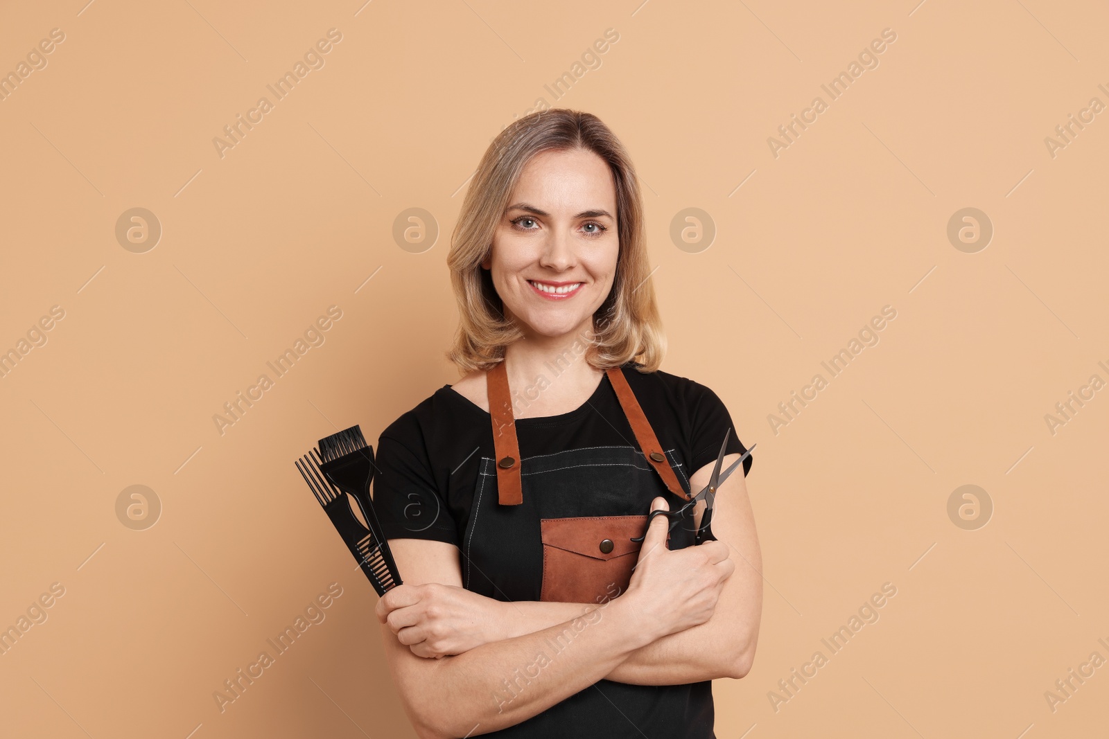 Photo of Smiling hairdresser with combs and scissors on beige background