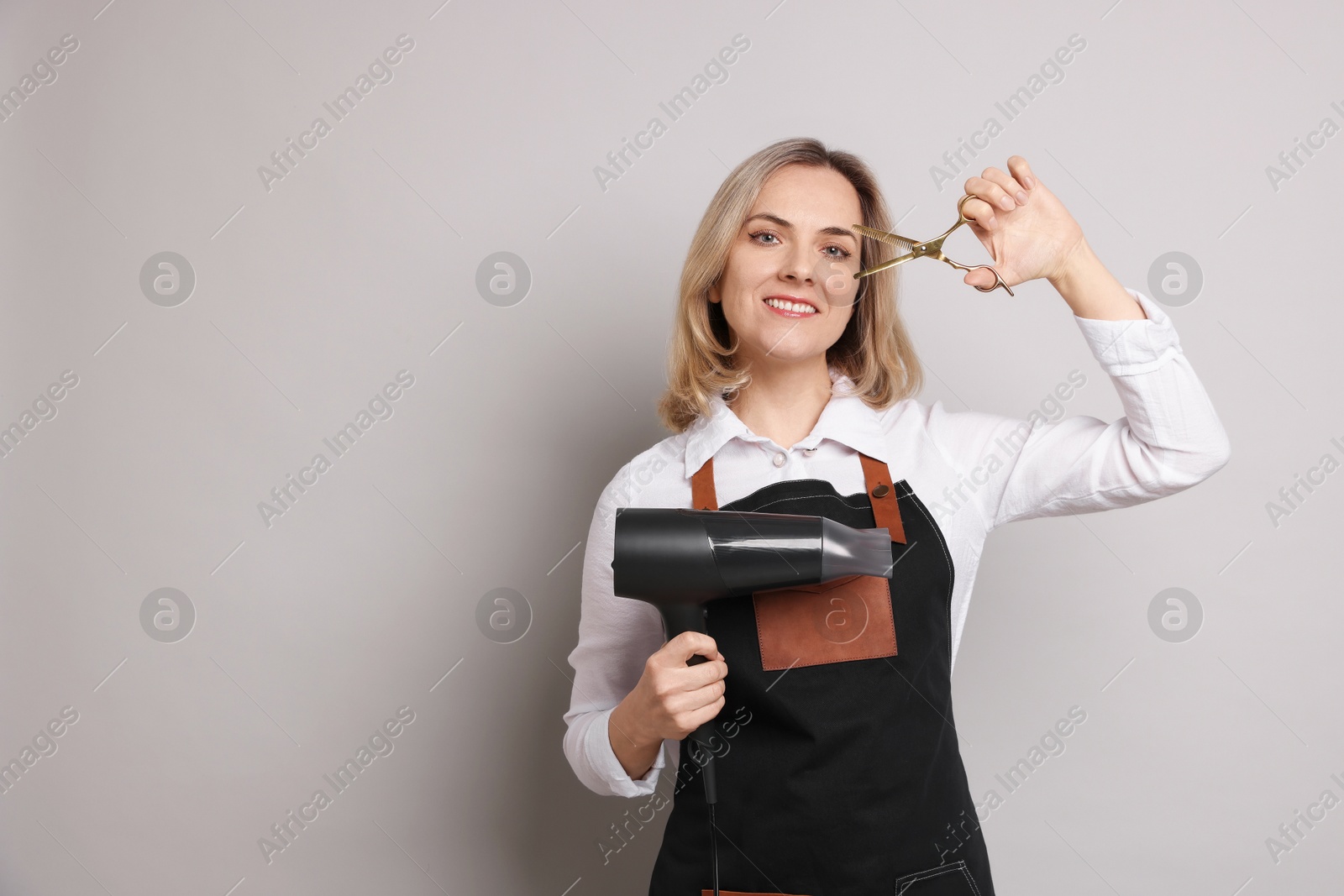 Photo of Smiling hairdresser with dryer and scissors on gray background, space for text