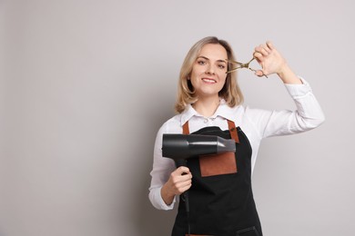 Smiling hairdresser with dryer and scissors on gray background, space for text