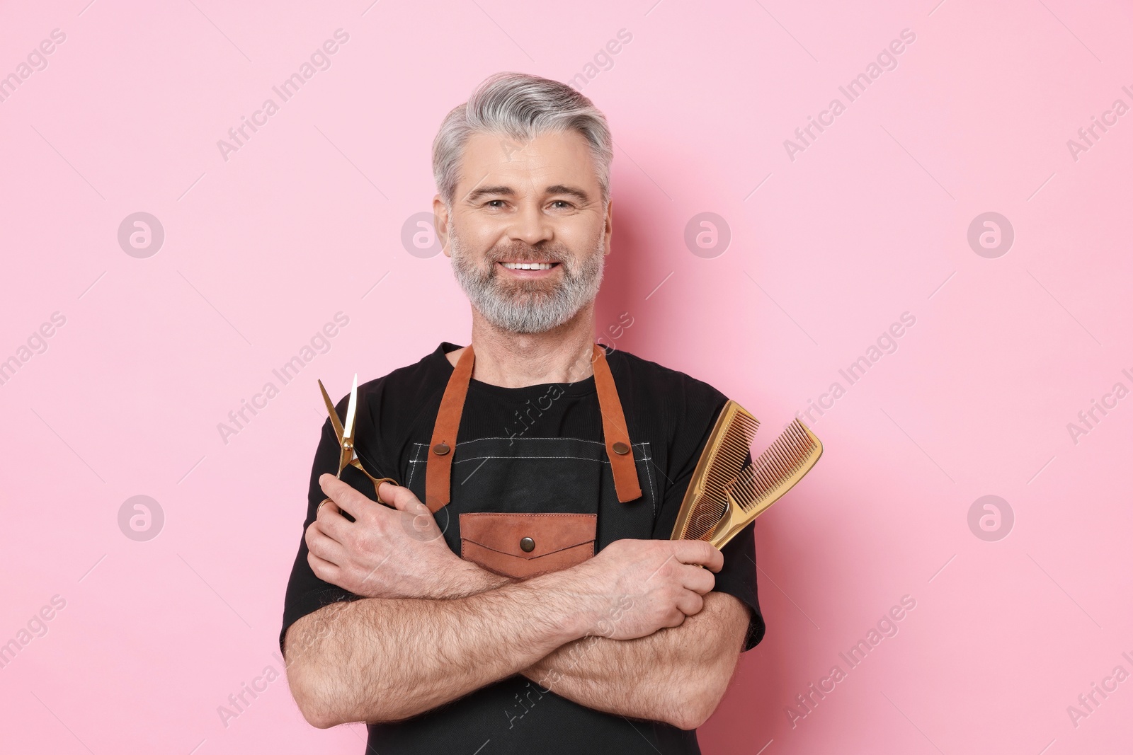 Photo of Smiling hairdresser with scissors and combs on pink background