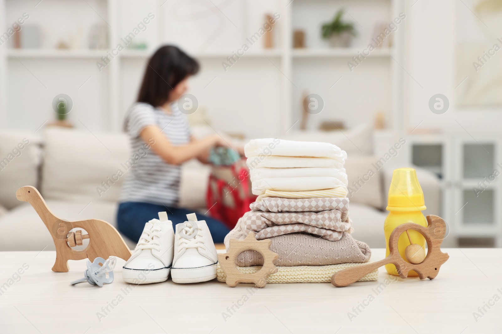 Photo of Baby's stuff on white table and mother packing bag, selective focus