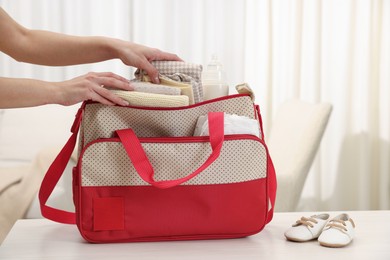 Photo of Mother packing baby's stuff into bag at white table, closeup