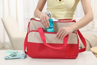 Photo of Mother packing baby's stuff into bag at white table, closeup