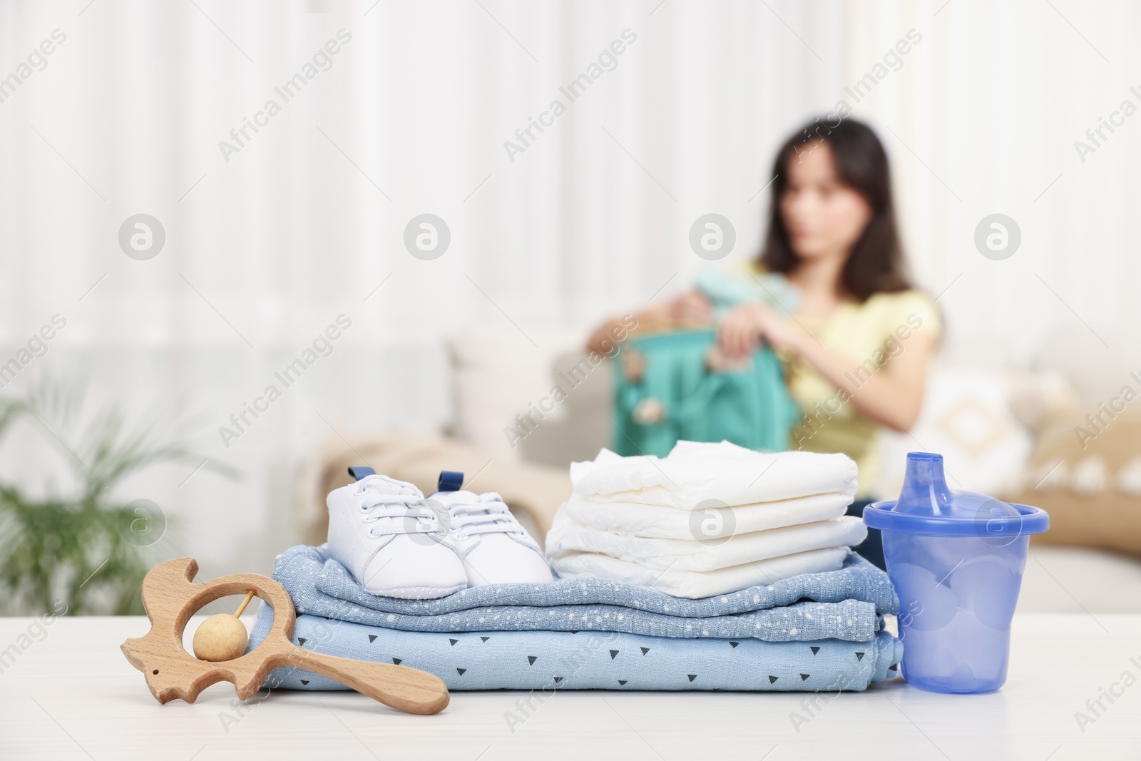 Photo of Baby's stuff on white table and mother packing bag, selective focus