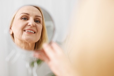 Photo of Smiling middle aged woman with round mirror on blurred background