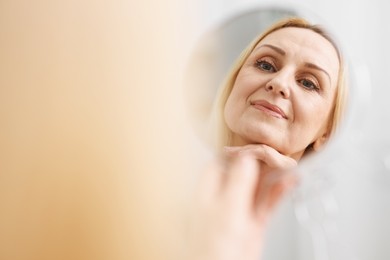 Beautiful middle aged woman with round mirror on blurred background