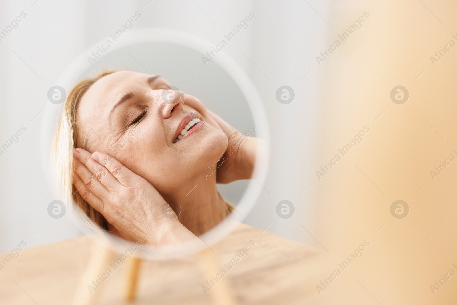 Photo of Smiling middle aged woman near round mirror on blurred background. Space for text