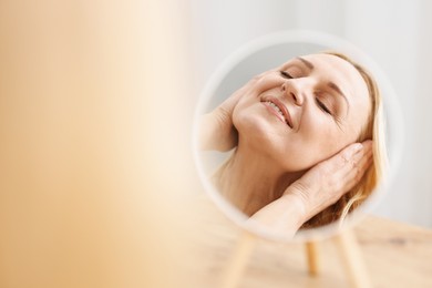 Photo of Smiling middle aged woman near round mirror on blurred background. Space for text